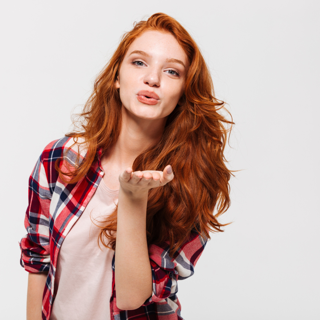 Красивая рыжеволосая девушка шлет воздушный поцелуй