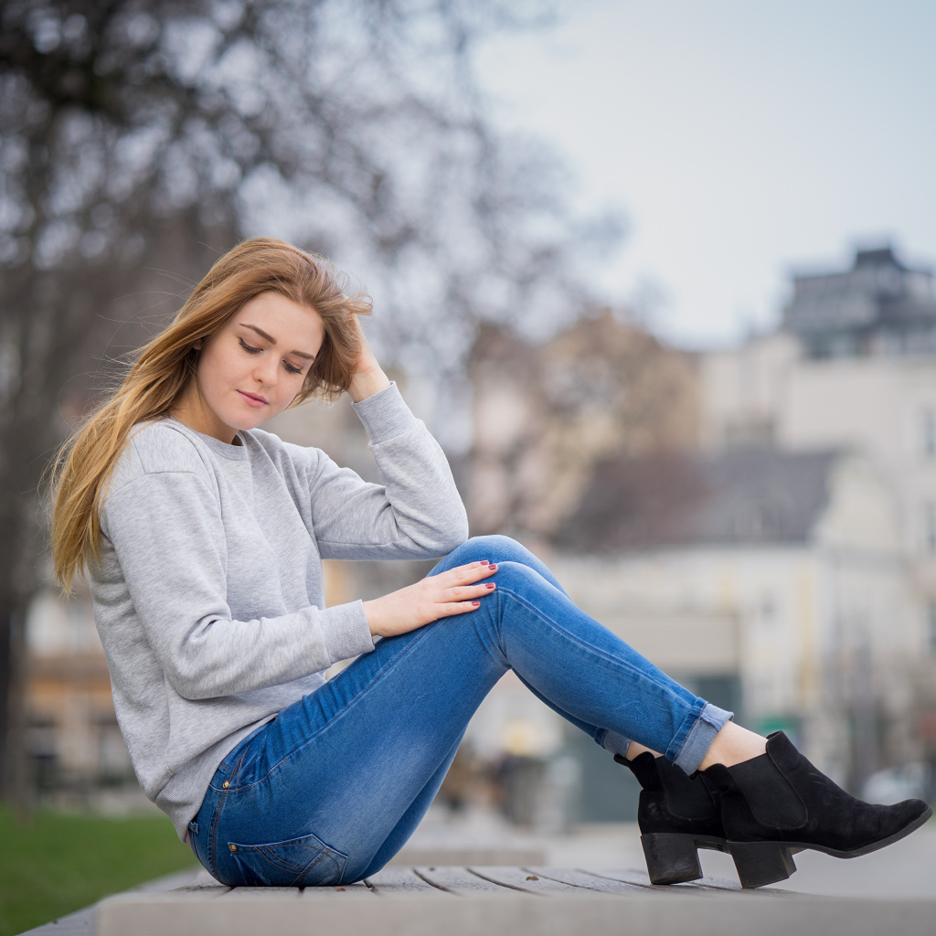 Милая девушка в синих джинсах сидит на лавке