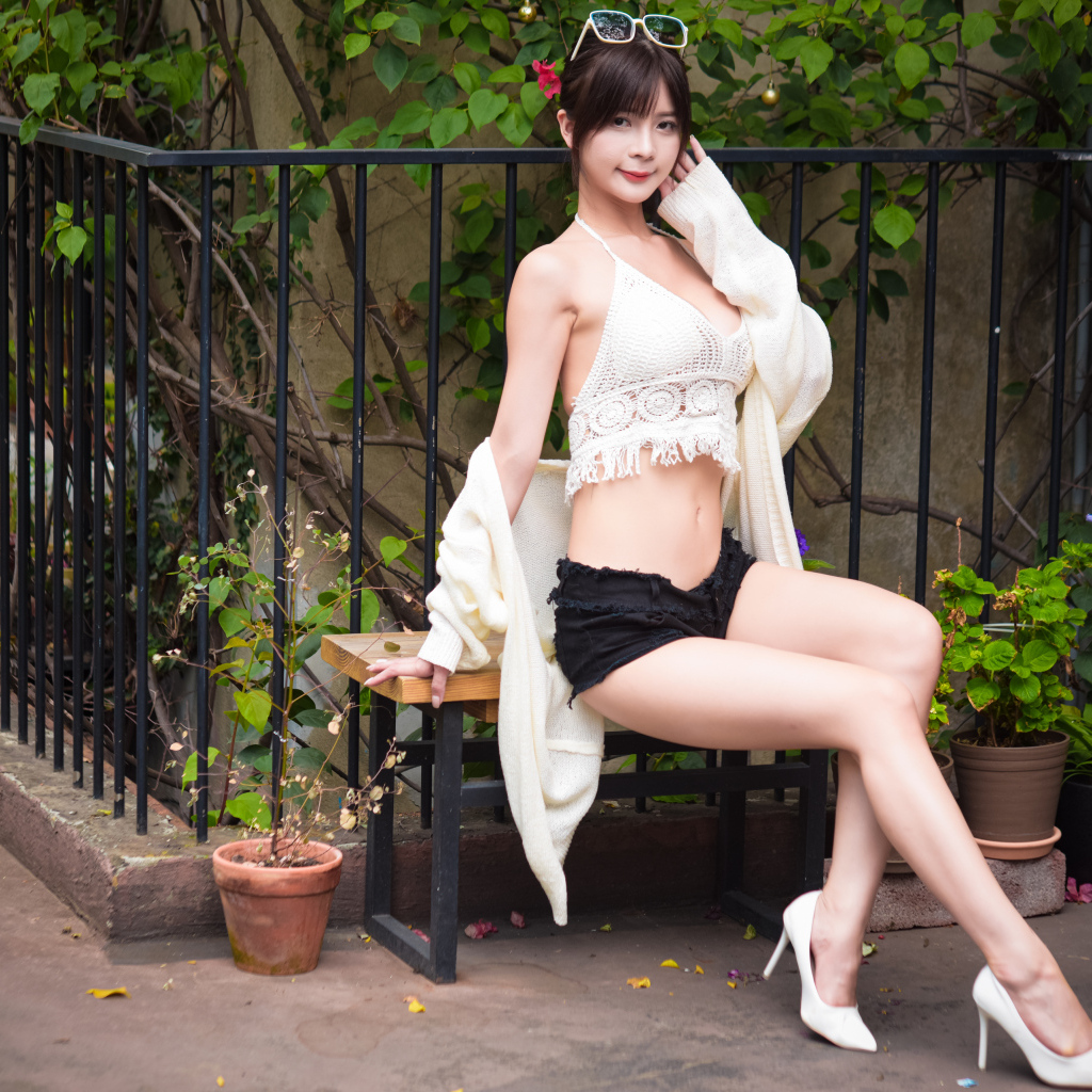 Стройная девушка азиатка сидит на лавке у дома