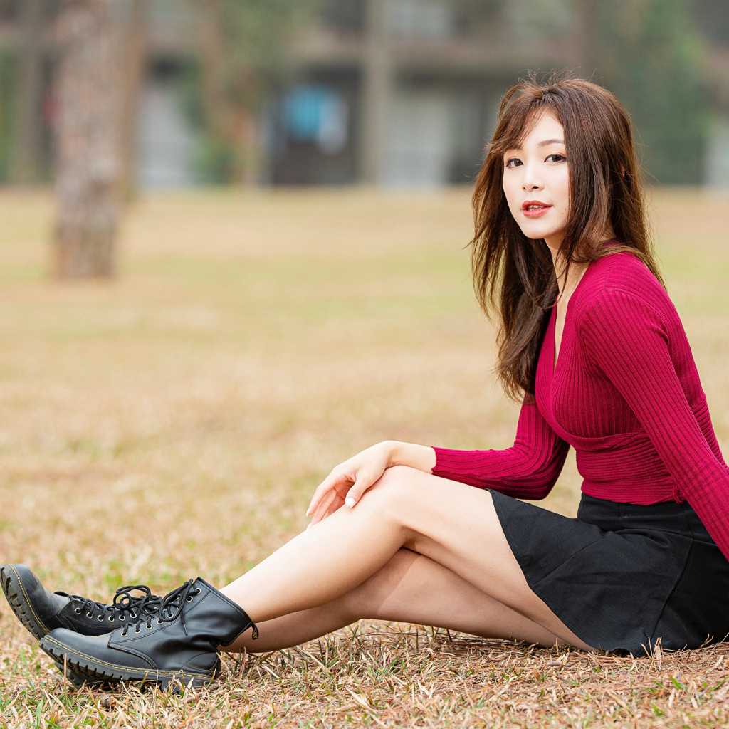 Молодая азиатка в красном свитере сидит под деревом