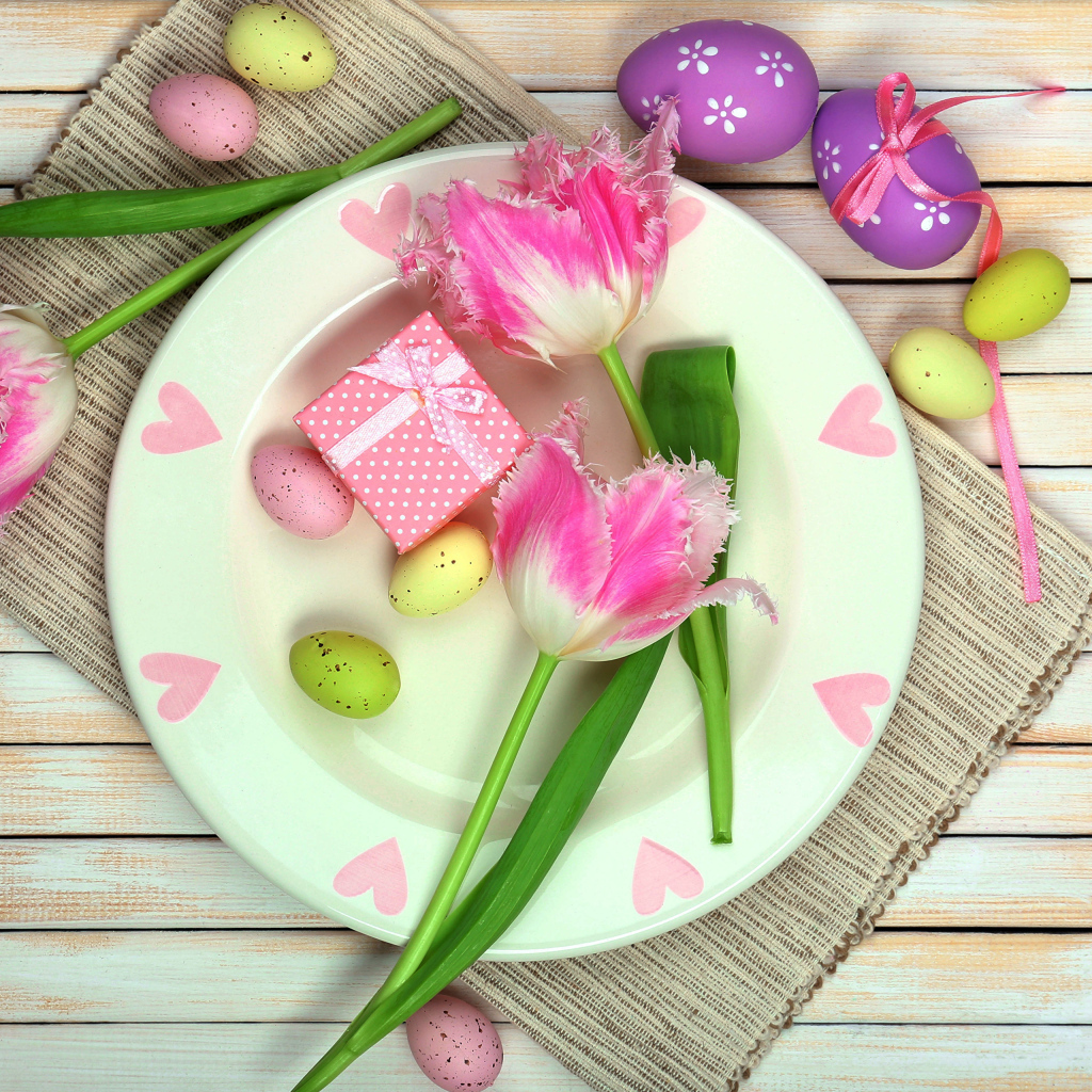 Пасхальные яйца с тюльпанами на тарелке на столе