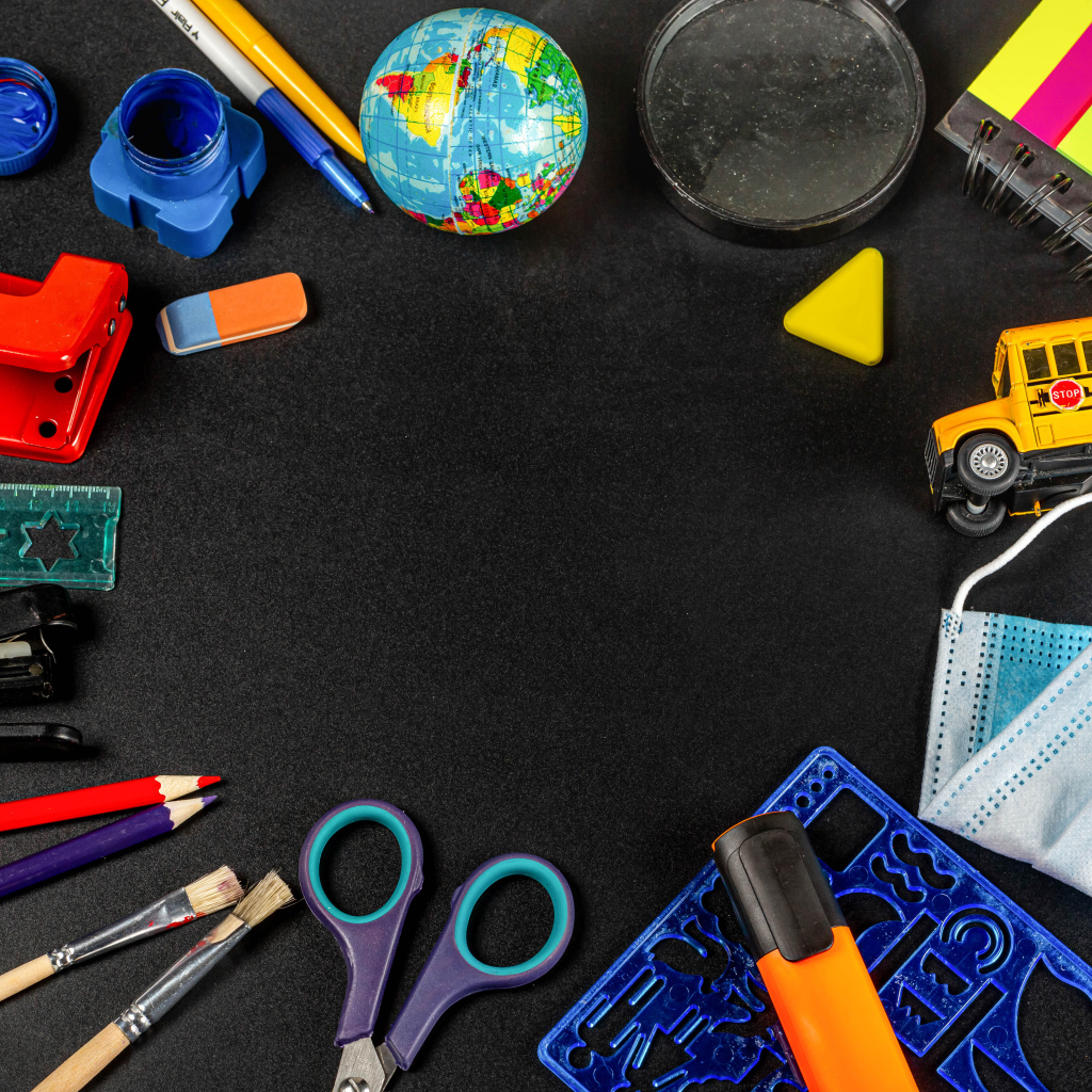 Канцелярские предметы, глобус и игрушечный автобус на черном фоне