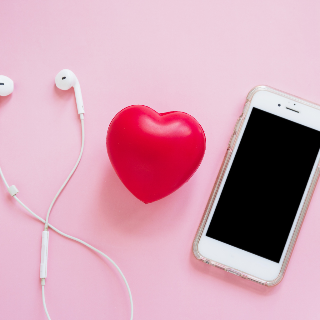 Телефон, наушники и красное сердце на розовом фоне