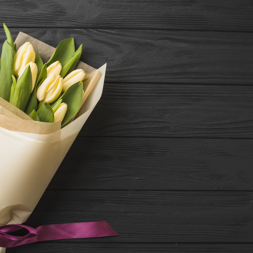 Букет желтых тюльпанов в бумаге на черном столе