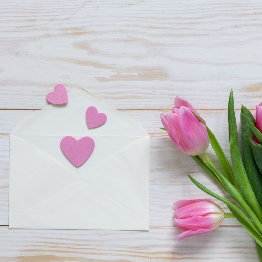 Розовые тюльпаны с конвертом с сердечками на деревянном фоне