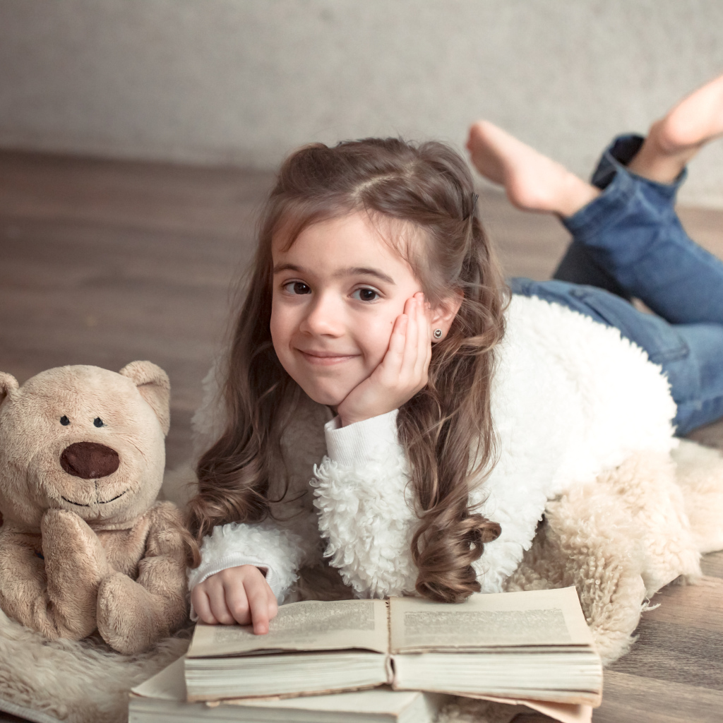 Девочка с медведем и книгой лежит на полу