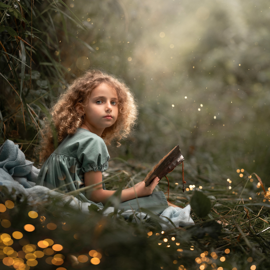 Милая девочка читает книгу сидя на траве