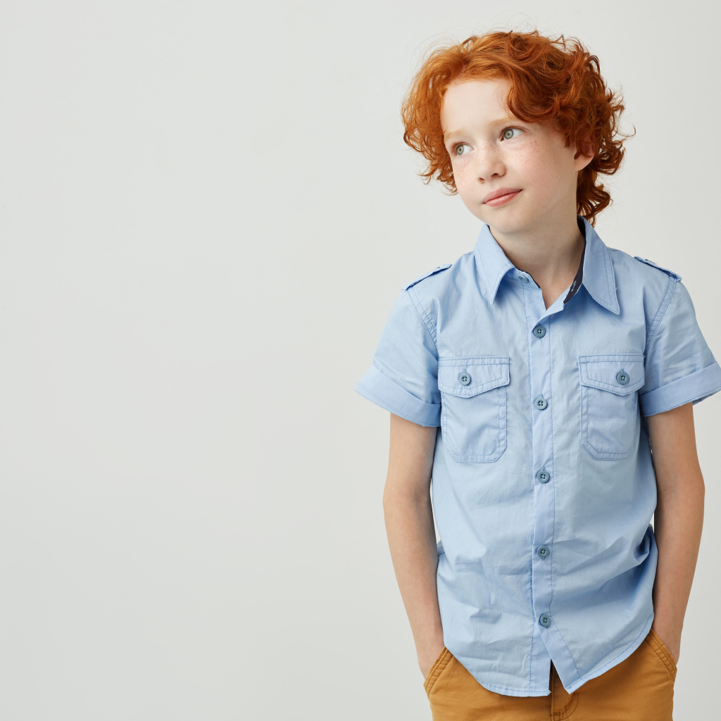 Рыжеволосый мальчик на фоне серой стены