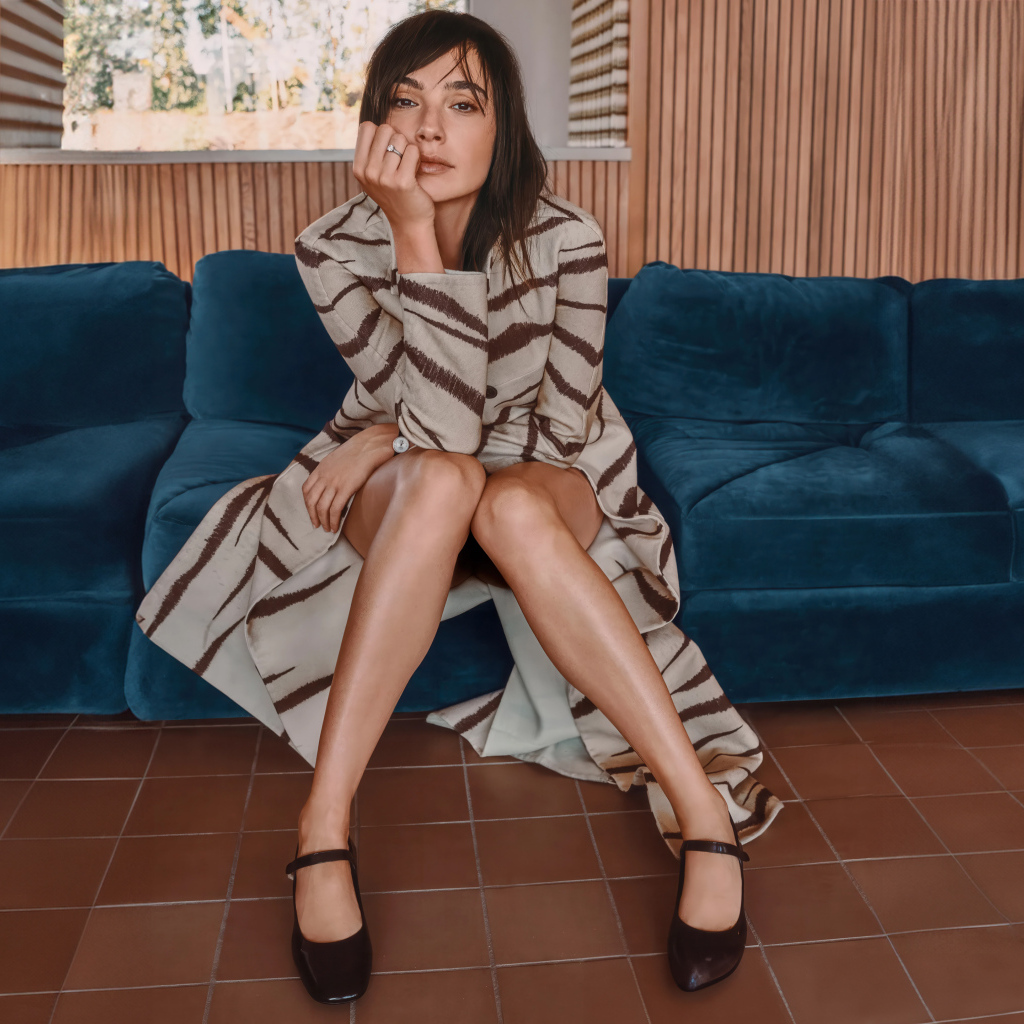 Актриса Галь Гадот в пальто сидит на диване