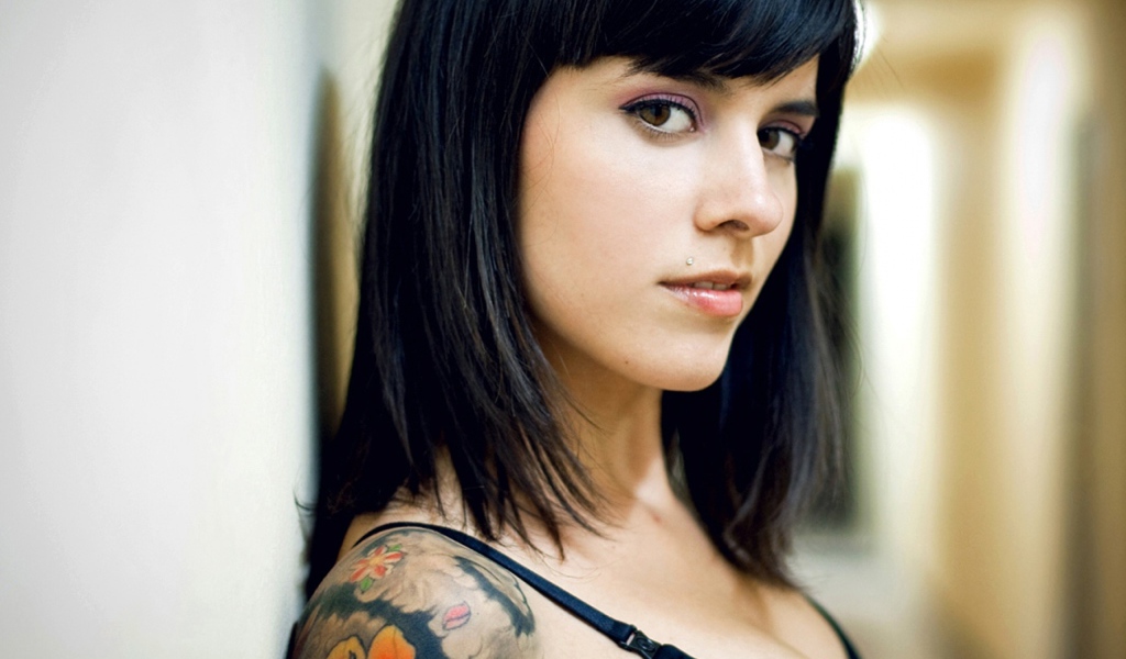 Девушка брюнетка с пирсингом в губе и татуировкой на плече