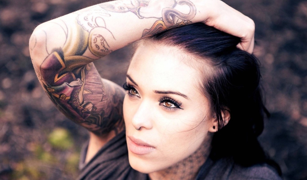 Девушка брюнетка с пирсингом в носу и татуировкой на руке