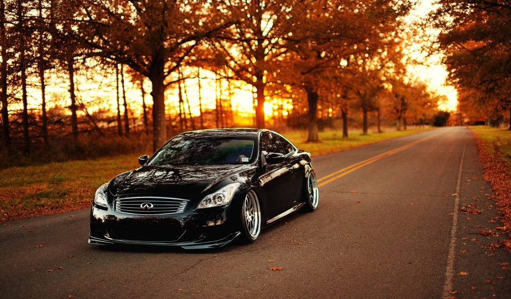 Черный Infiniti на шоссе среди осенних деревьев