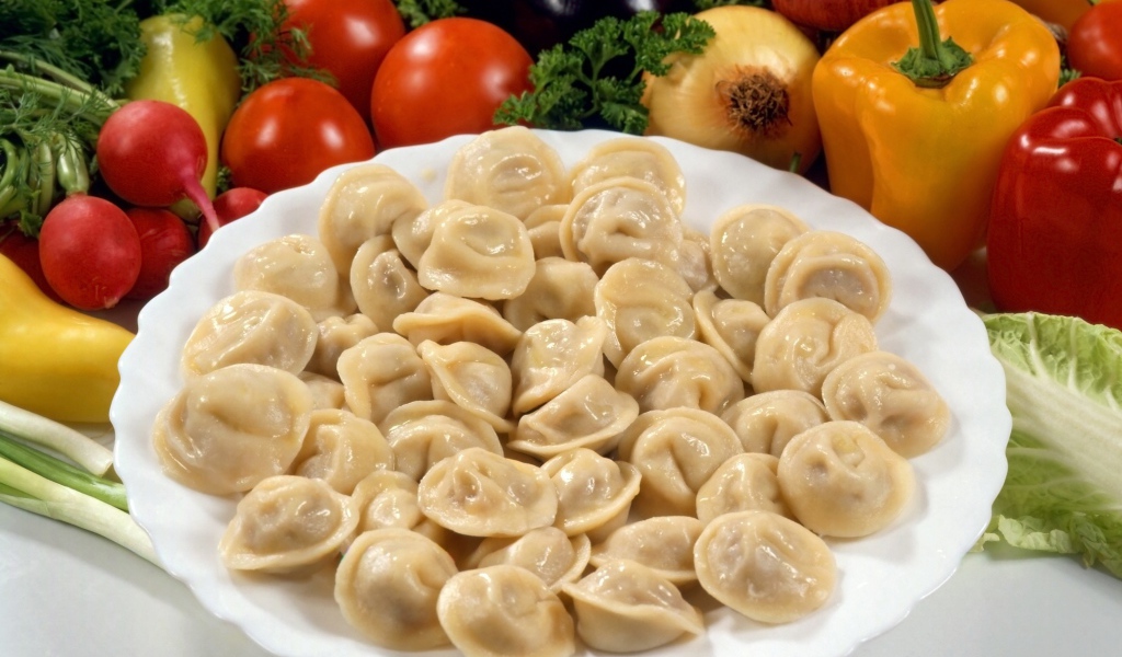 Пельмени на тарелке среди овощей