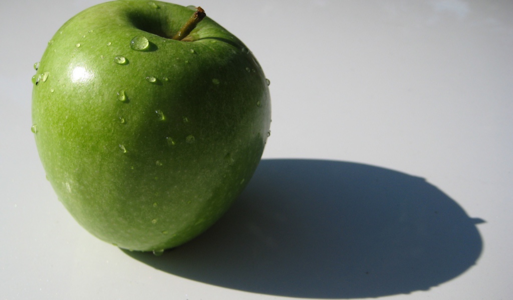 Зеленое яблоко на белой поверхности