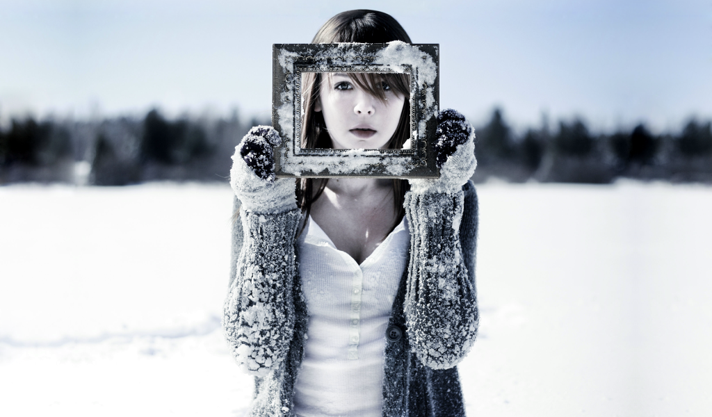 Девушка держит в руках фоторамку в снегу