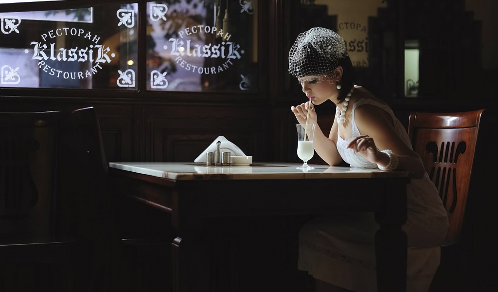 Девушка в белом платье пьет коктейль в ресторане