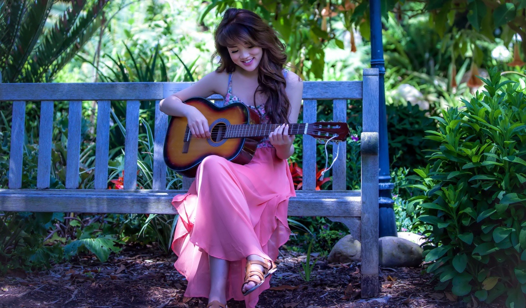 Девушка сидит на скамье в саду и играет на гитаре