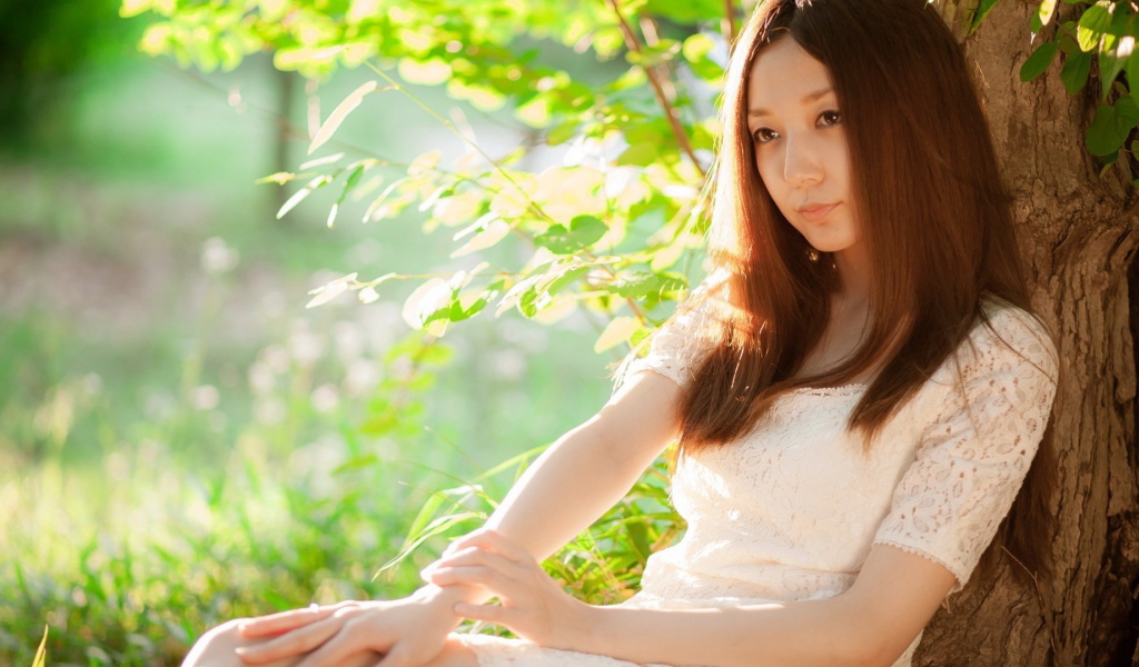 Азиатская девушка прислонилась спиной к дереву