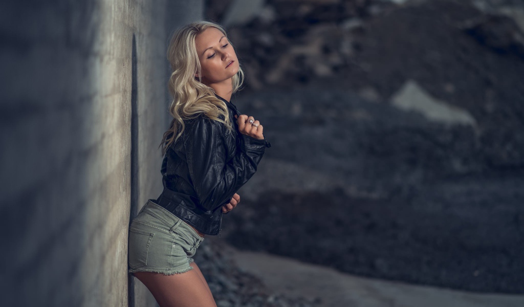 Блондинка в джинсовых шортах стоит у стены
