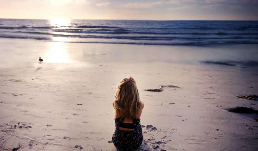 Блондинка в платье сидит на пляже