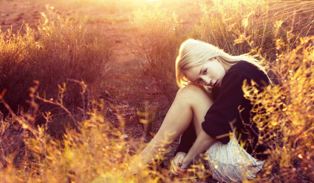 Блондинка сидит среди кустарников