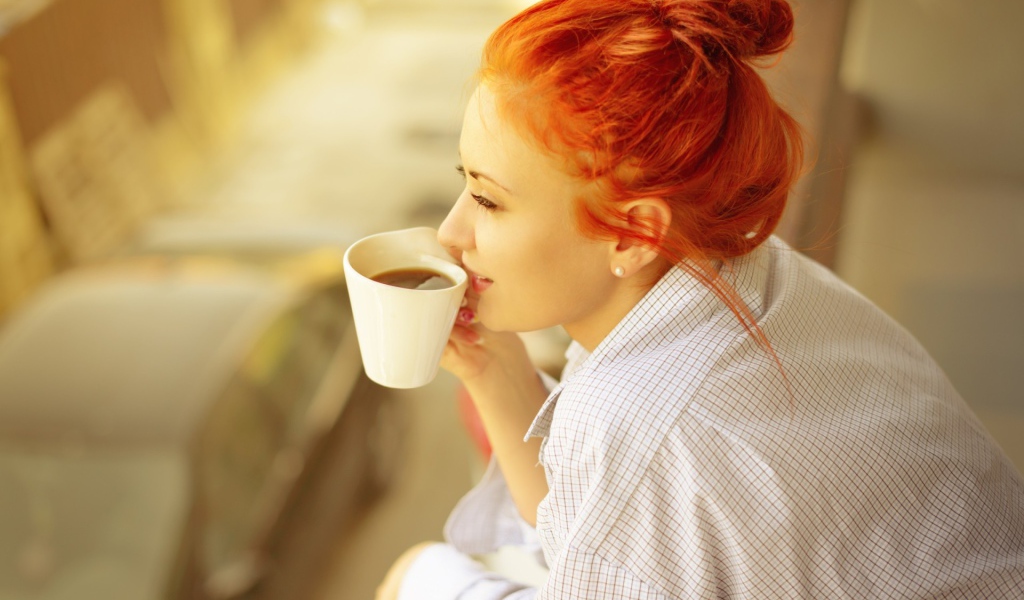 Ярко рыжая девушка в рубашке пьет кофе