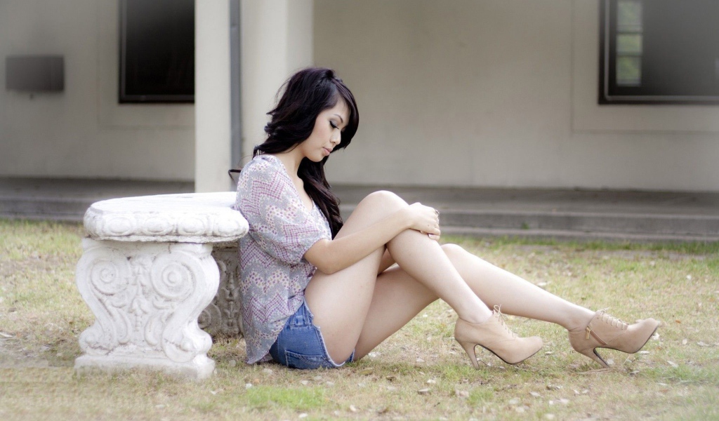Brunette sitting on the ground near a stone bench