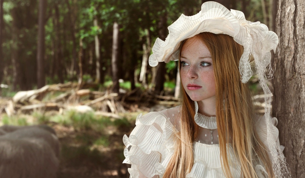 Веснушчатая девушка в белой шляпке стоит у дерева