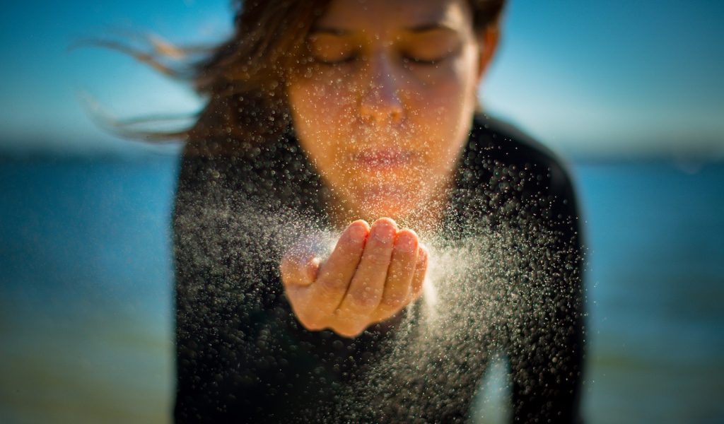 Девушка сдувает песок с руки