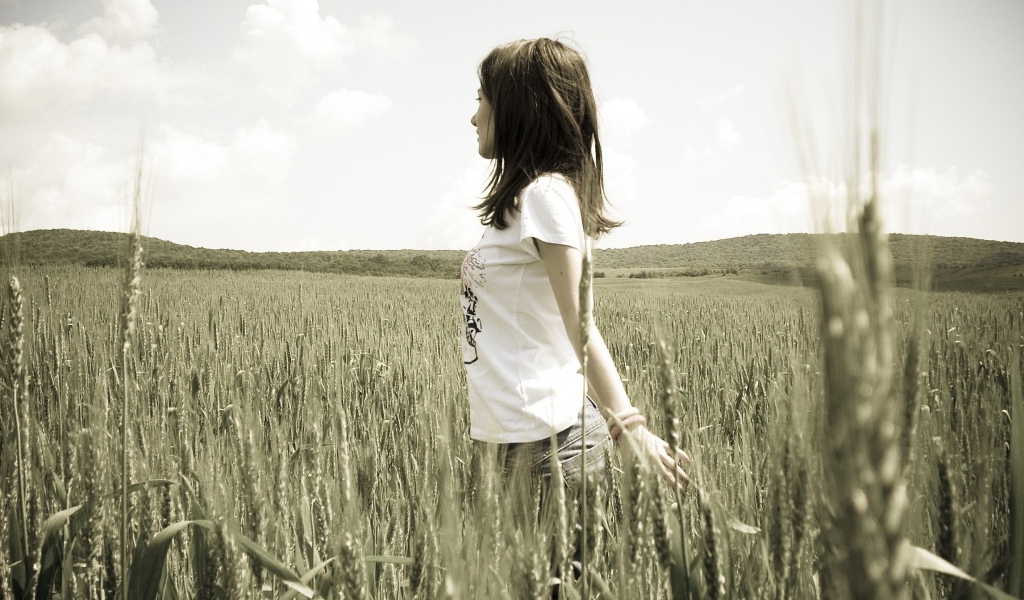 Девушка в белой футболке гуляет по пшеничному полю