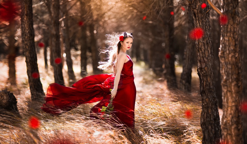 Девушка в красном платье стоит в ветренном лесу