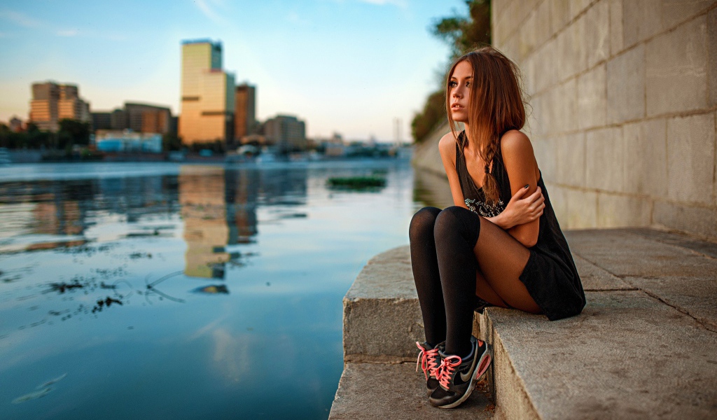 Girl in sneakers sitting on the embankment