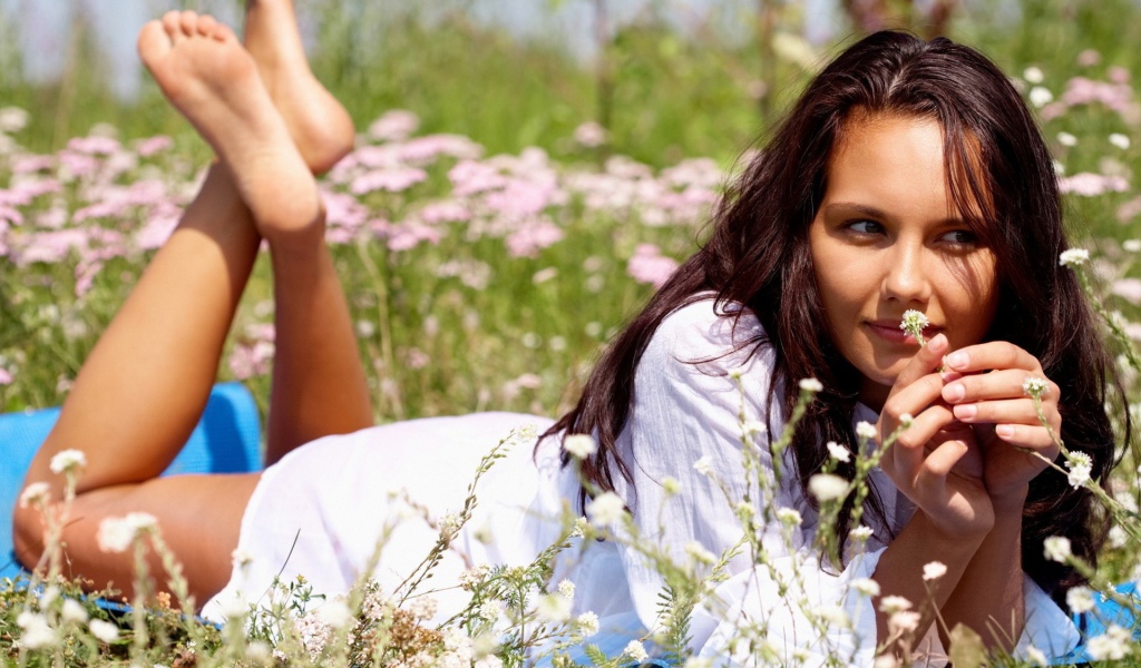 Девушка лежит на животе и держит в руке белый цветок