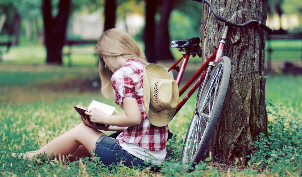 Девушка читает книгу сидя в парке на газоне
