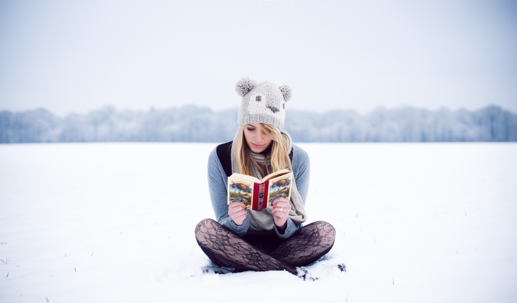 Девушка читает книгу сидя на снегу