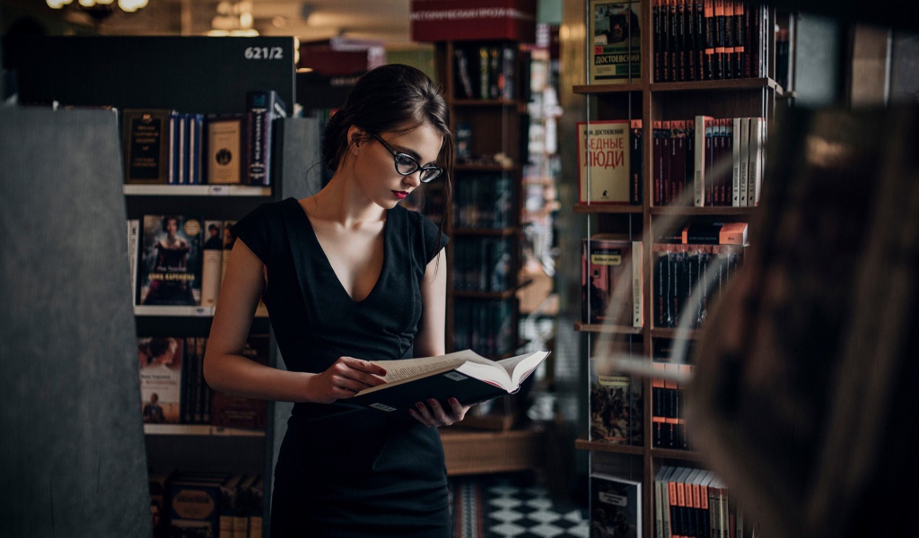 Девушка читает среди книжных полок