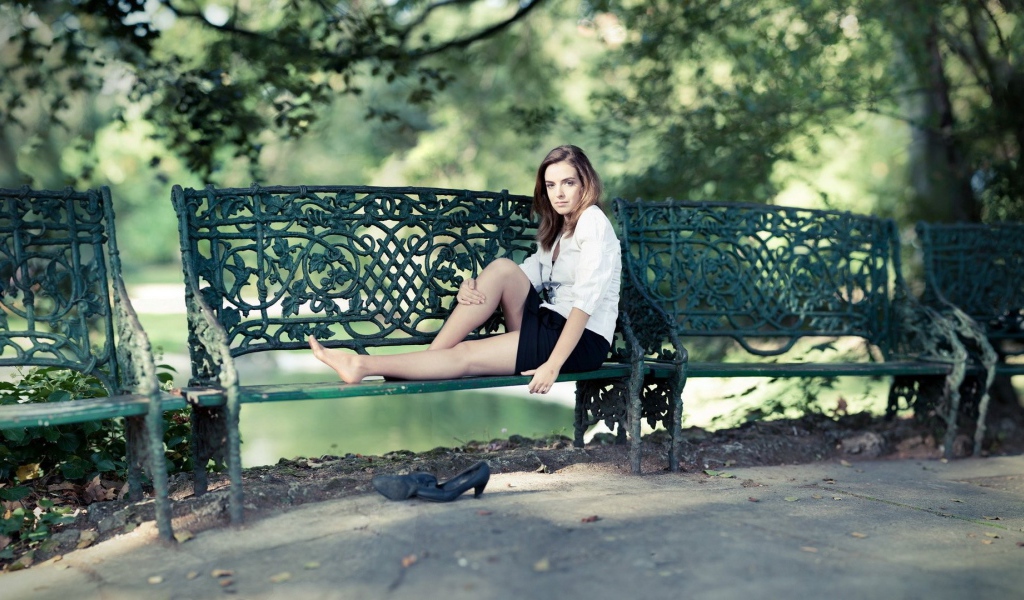 Девушка сидит на кованной парковой скамье