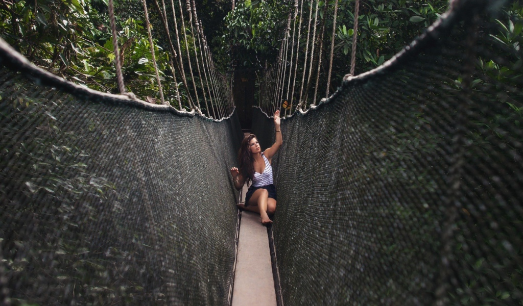 Девушка сидит на подвесном мосту