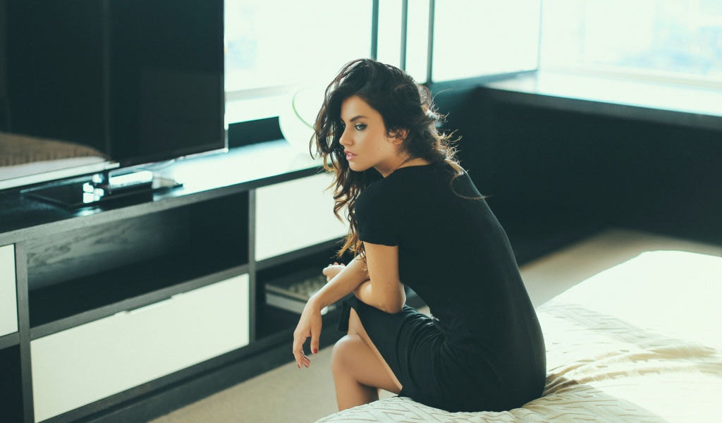 Девушка сидит на кровати перед телевизором