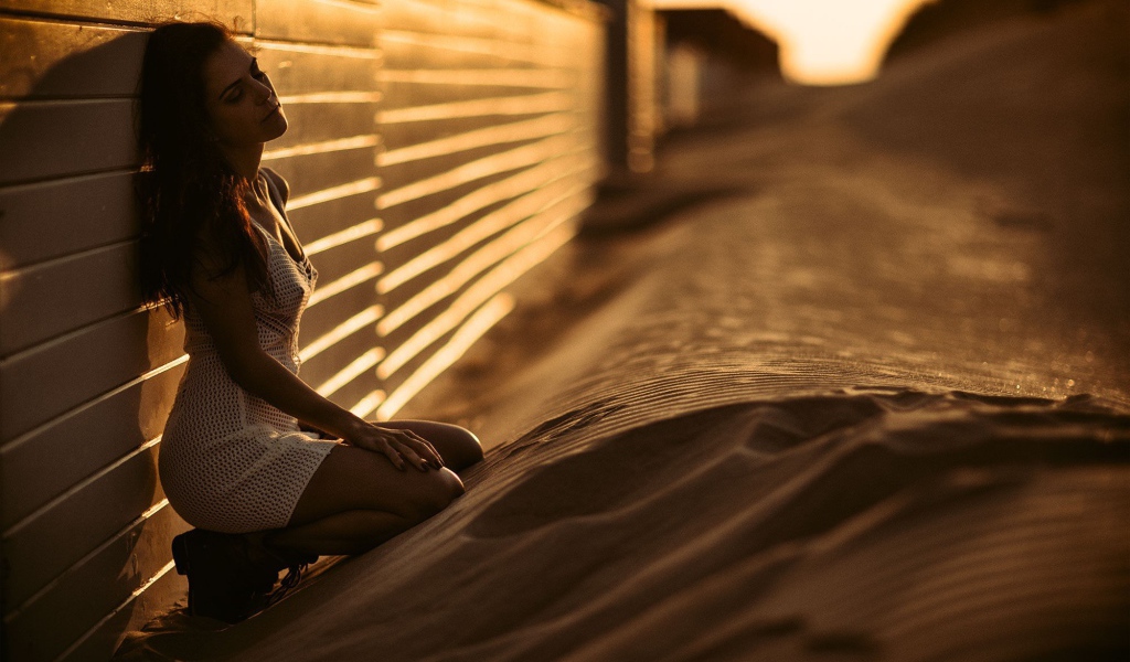 Девушка сидит на песке у забора