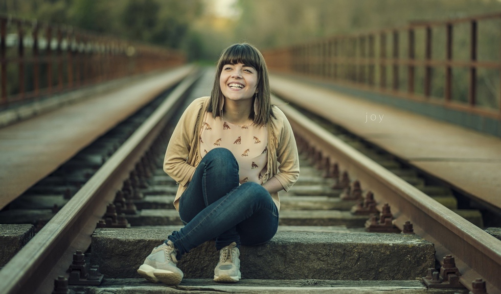 Девушка улыбается сидя на рельсах