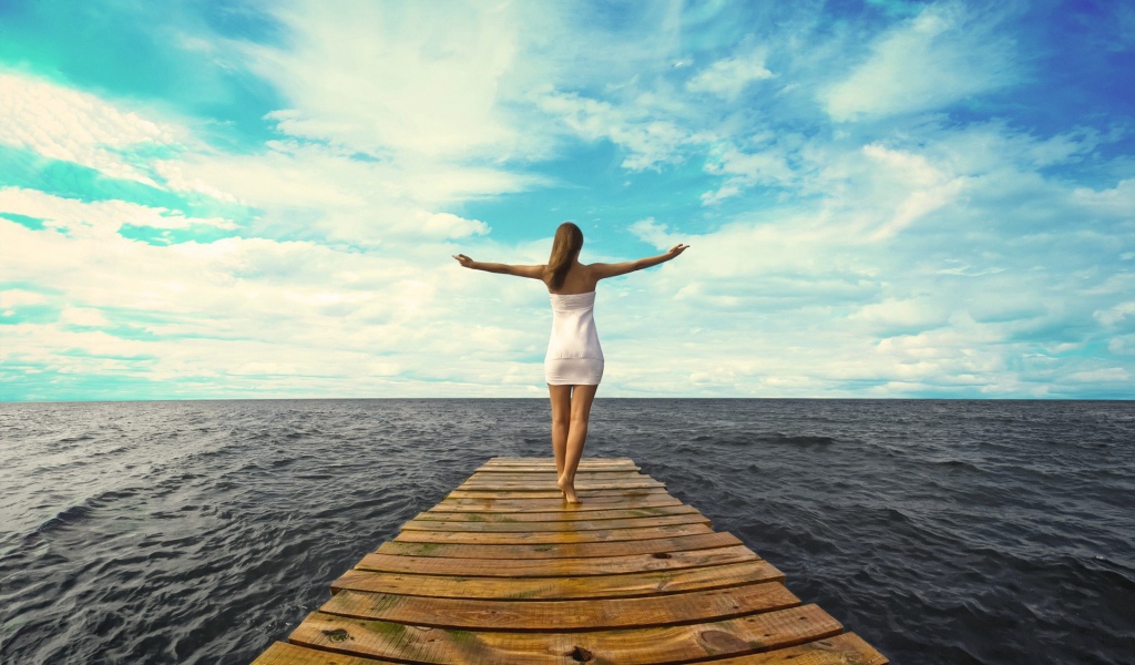 Девушка стоит раскинув руки на краю причала