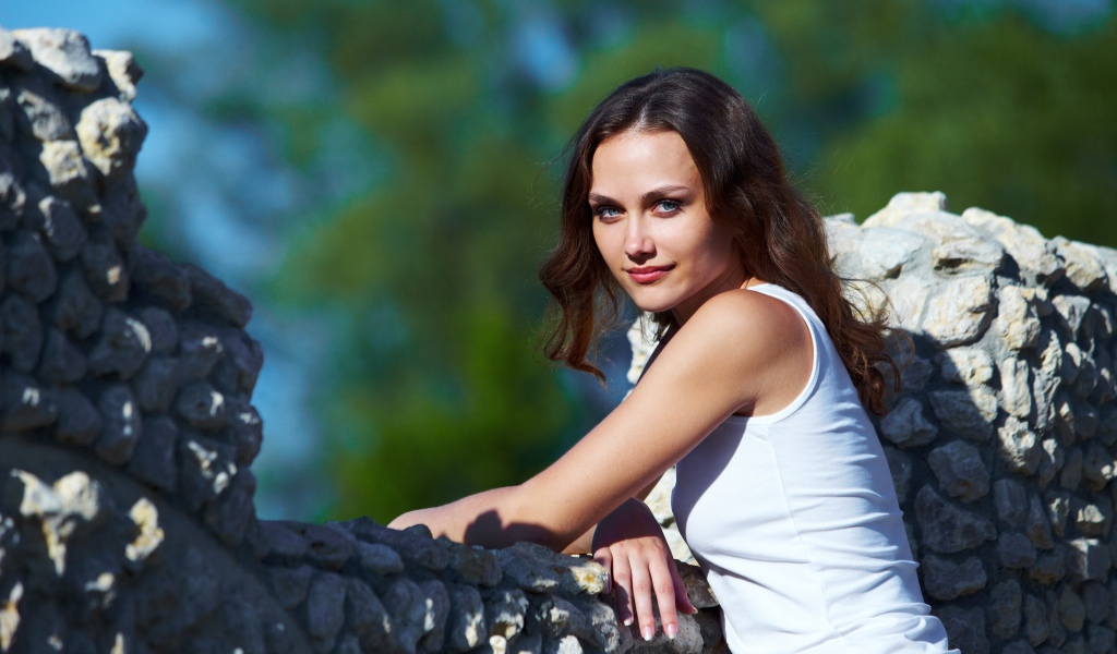 Девушка стоит у забора из камня