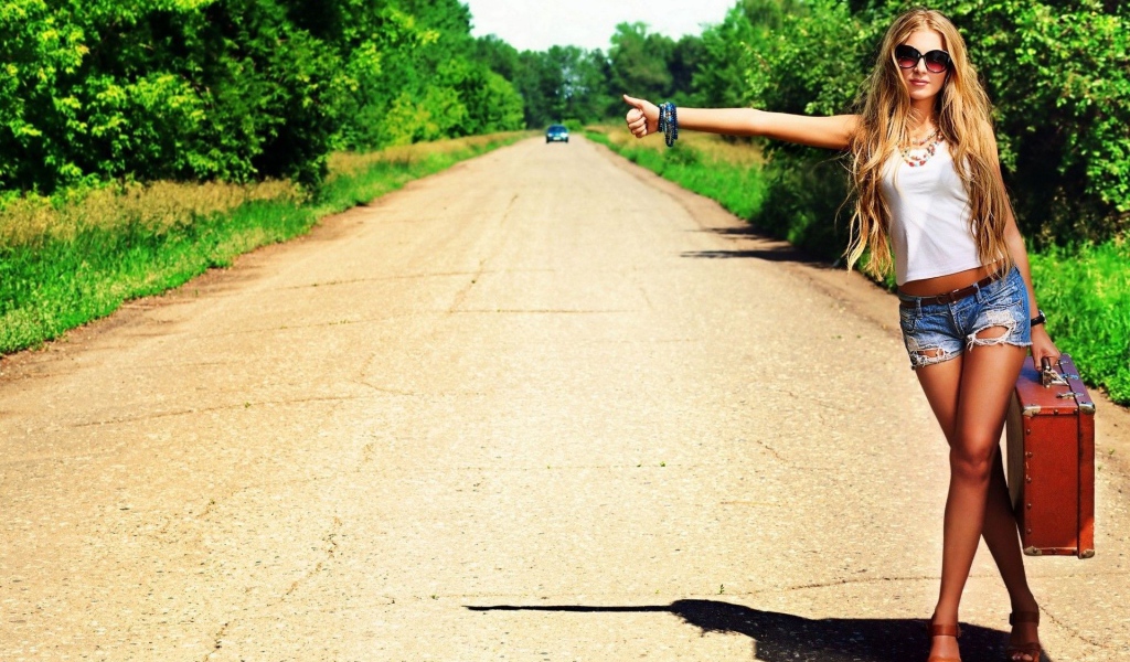 Девушка с чемоданом занимается автостопом