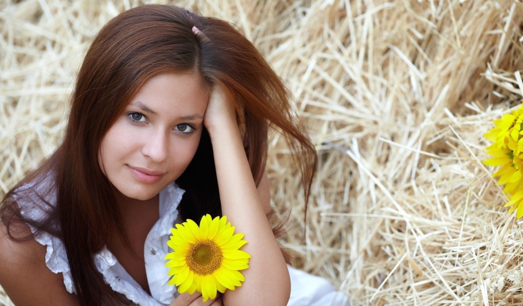 Девушка с желтым цветком сидит на сене