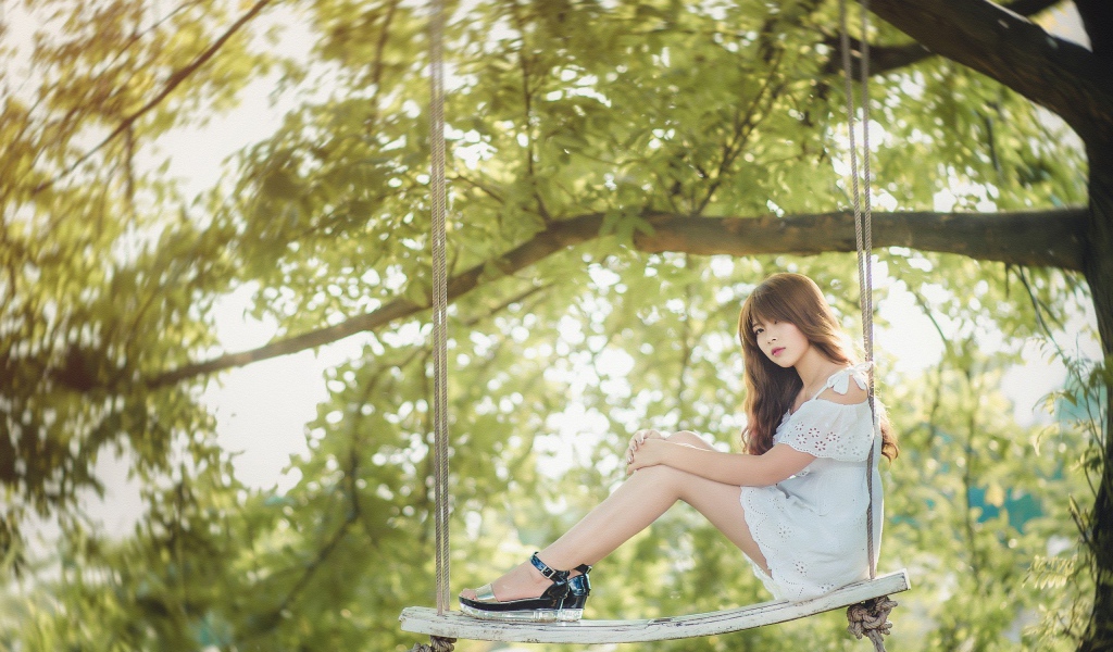 Японская девушка в белом платье сидит на качелях