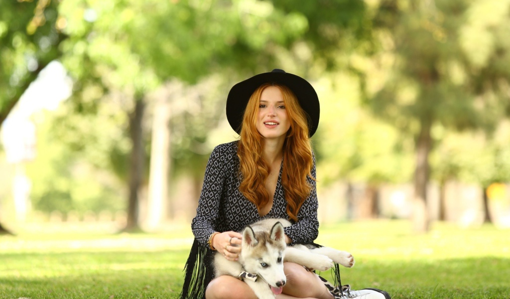 Рыжеволосая девушка в шляпе ласкает щенка хаски