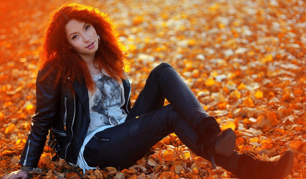 Рыжая девушка сидит на ковре из желтых листьев