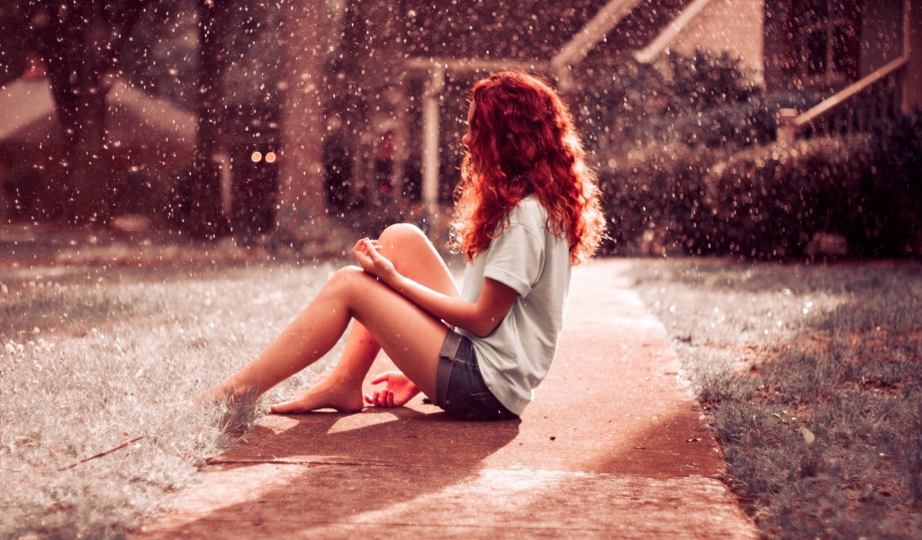 Рыжая девушка сидит на земле во время дождя