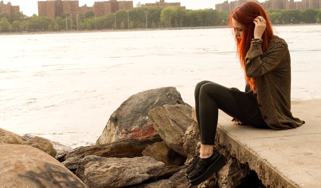 Рыжая девушка сидит на плитах набережной